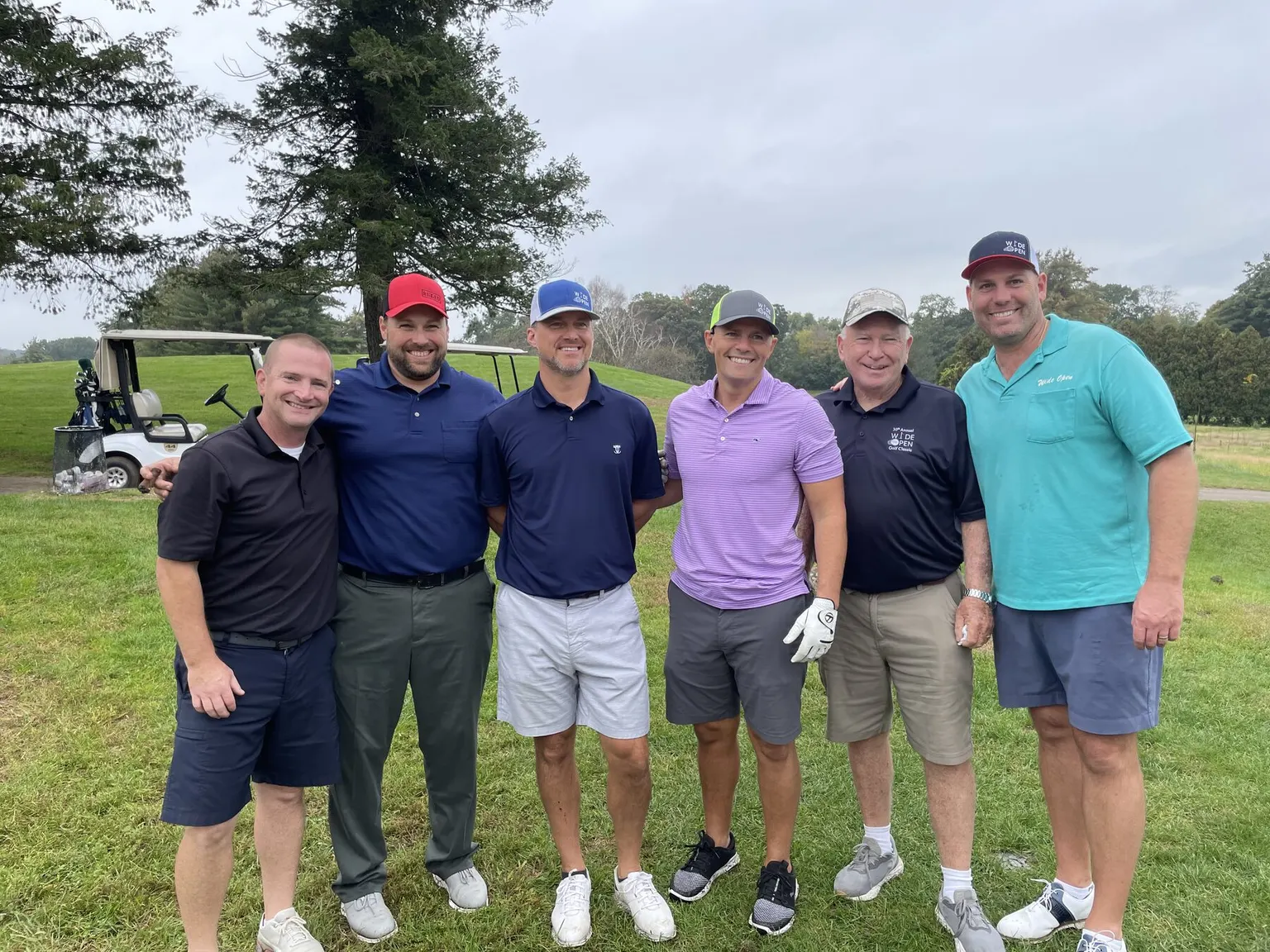 Four golfers kneeling together on the fairway at the Wide Open Golf Classic